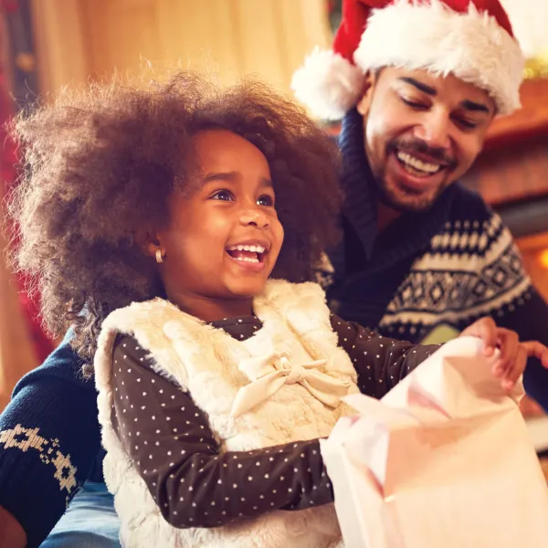 Smiling man in Santa hat watching smiling child open a present