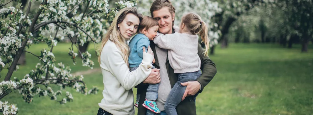 A family standing and hugging in a park with white trees