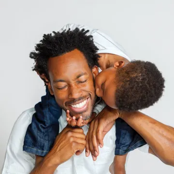 Son on dads shoulders kissing his cheek