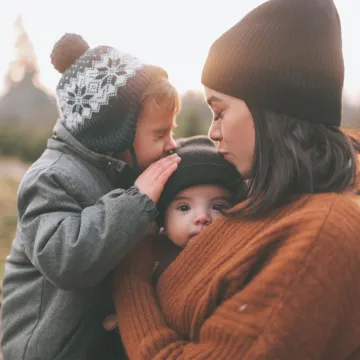 Woman outside holding two children and kissing one on the head