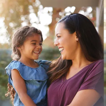 Mom holding her daughter outside smiling 