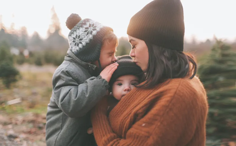 Woman outside holding two children and kissing one on the head